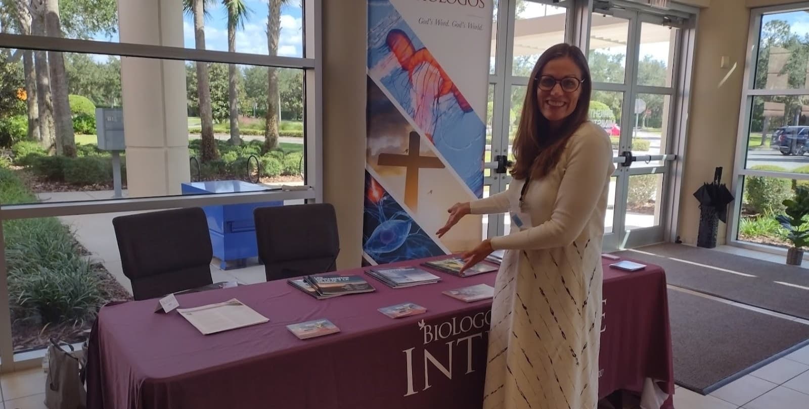 A woman stands smiling in front of a BioLogos table at an event.