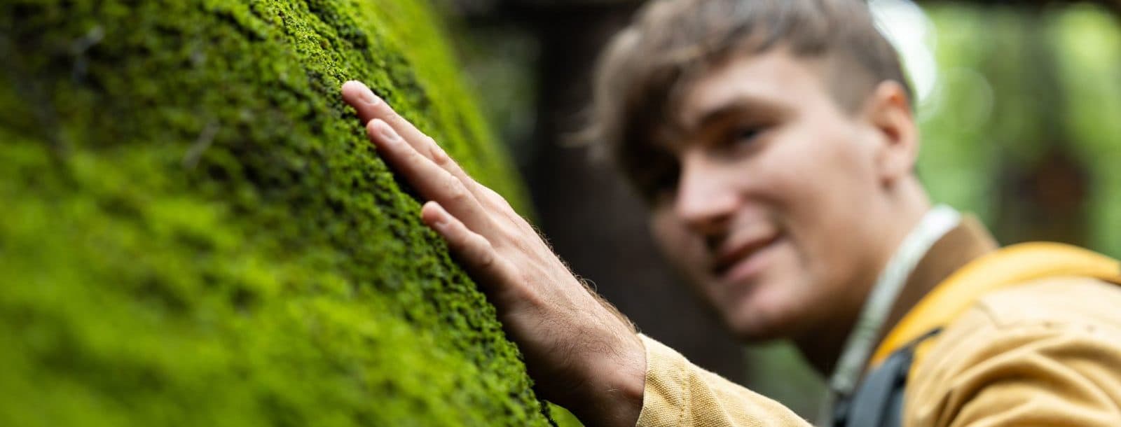 A man touches a mossy rock with his left hand.