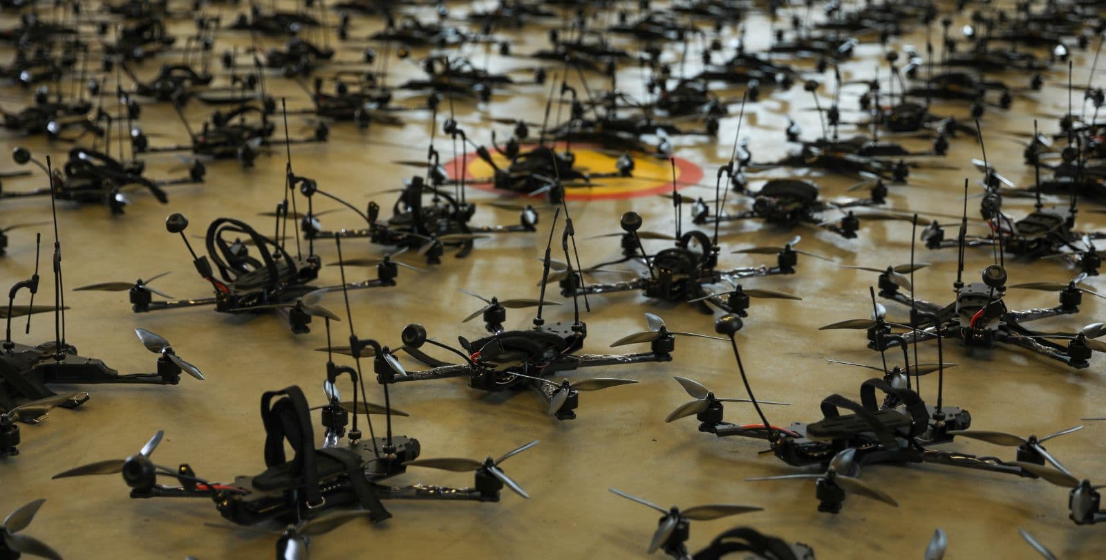 Dozens of small black drones sit on a cement floor.