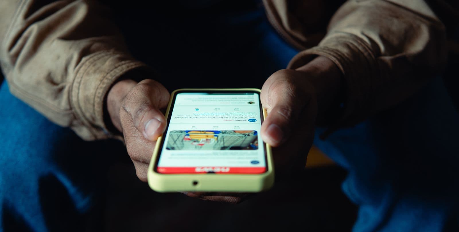Closeup of a man's hands holding a phone open to a news story.