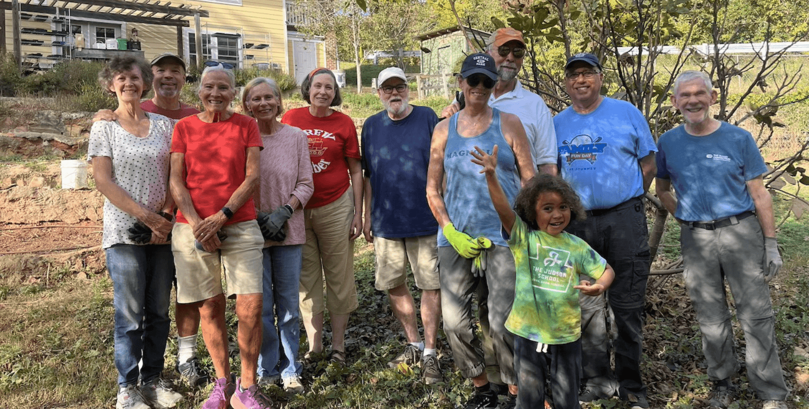 A group of 11 (10 adults and one child) stand together in a backyard.