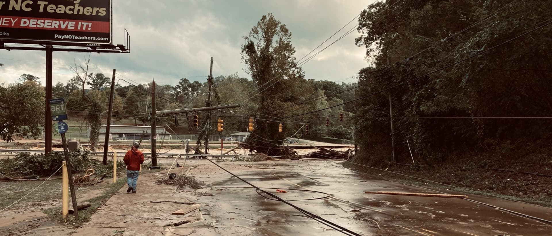 A road covered in downed trees and power lines. The sky above it is cloudy and grey.