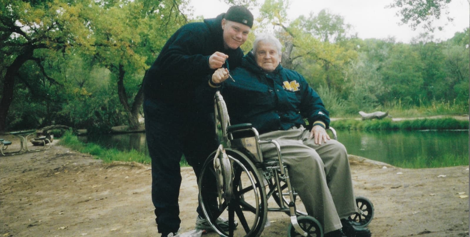 In a photo taken about 20 years ago, Andrew Black and his grandfather hold up a string of fish they caught near a river. Andrew stands next to his grandfather, who is seated in a wheelchair.