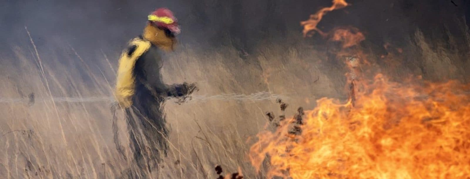 A person in protective gear starts a controlled blaze in a field.