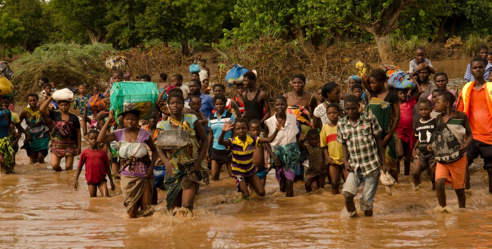 A crowd of people walk through knee-high water to evacuate a flood.