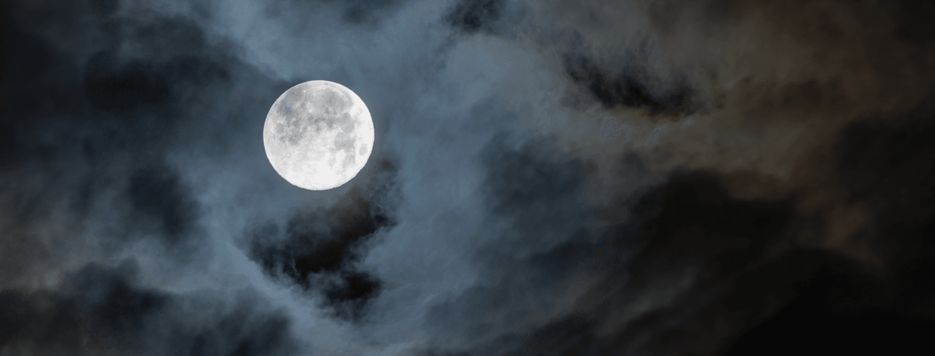A full Moon peaks through wispy clouds.