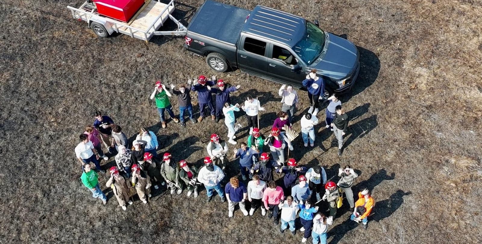 A group of 30 volunteers stand together in a field at the Little Bluestem Farm. A truck with trailer attached is behind them.
